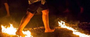 Primo piano di una persona che cammina a piedi nudi sui carboni ardenti durante un firewalking notturno. Camminata sui carboni ardenti - Rituale del fuoco e crescita personale.