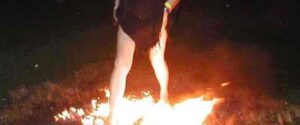 Persona che cammina attraverso fiamme vive su un letto di carboni ardenti durante una sessione di firewalking. Attraversamento del fuoco - Sfida e Potere Personale.